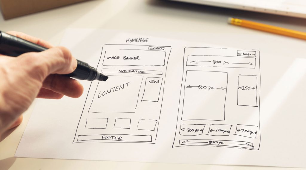 UX:UI Main tenant un feutre avec en arrière plan des schémas UX-UI Design